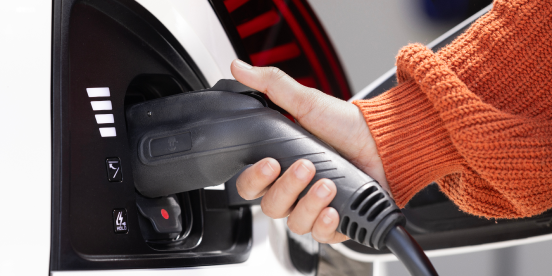 Person's hand connecting a charger to the charging port on their car